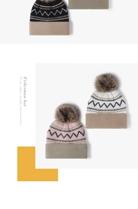 Detail of knit beanie with pompom showing black wavy patterns and ribbed cuff