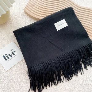 Detail of black winter scarf featuring fringe edges and white self-service woven label
