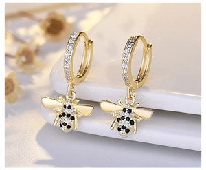 Macro detail of golden honey bee earrings with black and white rhinestones on white surface