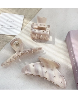 Detail of beige acetate hair claws with delicate rhinestone flower patterns on fabric