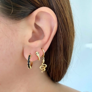 Close-up of gold snake earrings set with zircon stones on a female model ear