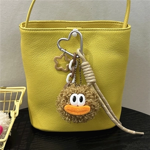 Detail of cute brown plush doll pendant with white eyes on yellow leather bucket bag