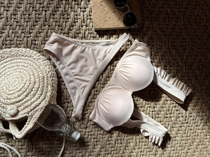 Detail view of beige bikini with ruffled cups and frill straps on a woven straw mat