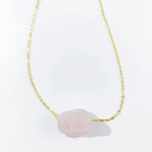 Detailed view of an irregular raw pink crystal stone pendant on a gold-tone chain necklace