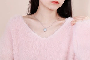 Detail of silver round shell pendant necklace on a model wearing a pink sweater