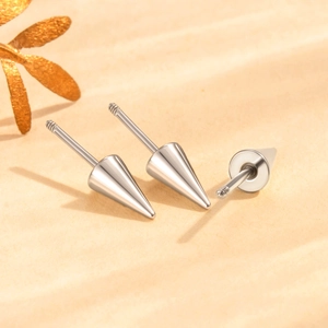 Surgical steel helix studs with cone spikes on textured background with golden leaves