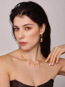 Detail of gold water-drop earrings and pink pearl necklace worn by a model in soft light