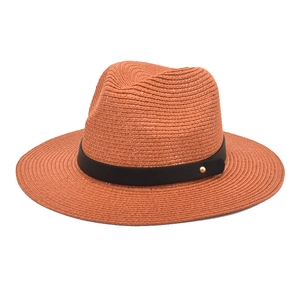 Detail of orange paper straw fedora hat featuring black leather band and gold metal rivet