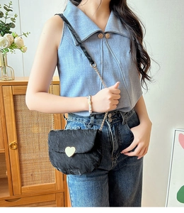 Détail d'un sac à bandoulière noir avec boucle coeur dorée et texture plissée