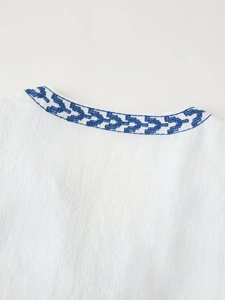 Detail shot of blue geometric embroidery on the collar of a white linen blouse