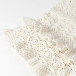 Close-up of cream white hollow-out knit fabric with elegant ruffle hem detailing