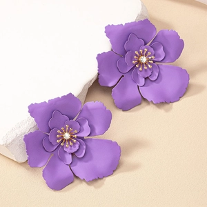 Close-up of matte purple floral earrings with gold stamens and sparkling crystal center