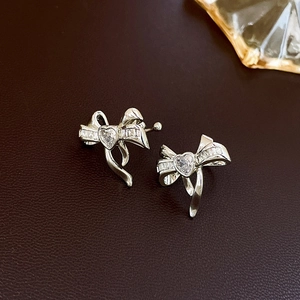Detailed view of silver bow-knot heart earrings with zircon inlay on a leather surface