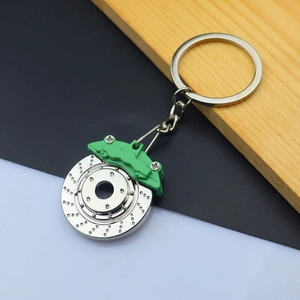 Detail of silver brake disc keychain with green caliper on wooden background
