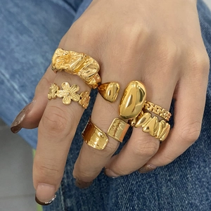 Stackable gold stainless steel rings with floral and lava textures on denim background