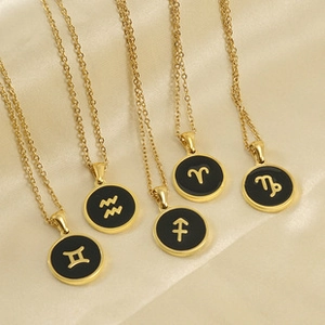 Close-up of five gold zodiac necklaces with black circular pendants on beige silk