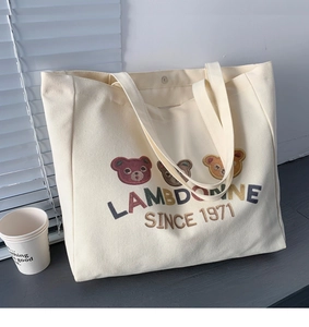 Close-up of embroidered cartoon bears and text on a beige canvas tote bag
