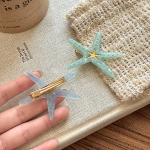 Detail of star-shaped hair clips in blue and green with gold alligator clips