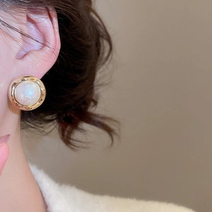 Close-up of gold plated geometric earrings with white pearls on a model ear