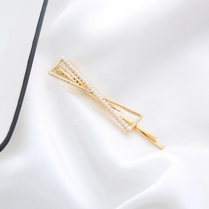 Detail shot of golden geometric hair clip with white faux pearls on white silk fabric