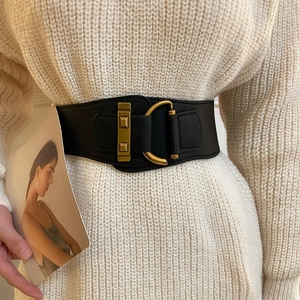 Close-up of black elastic wide belt with decorative gold buckles on a beige knit dress