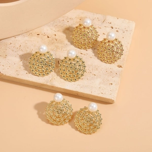 Detailed close-up of hollow gold earrings with pearls and colorful zircon stones on stone