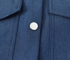 Detail of blue denim fabric texture and polished silver metal button with double stitching