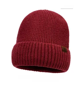 Detail of red cable knit beanie featuring a brown leather patch with snowflake motif