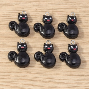 Detail of 6 black cat charms with glossy finish and metal rings on a wooden background