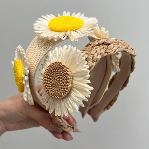 Detail of woven raffia headbands featuring large daisy floral ornaments in two colors