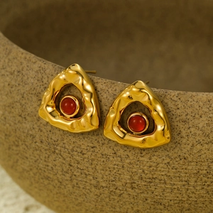 Detailed close-up of gold triangle earrings with red stone and hammered texture surface