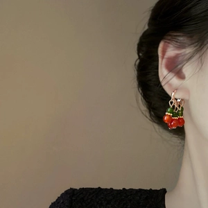 Ethnic style beaded earrings with red fruit charms and rose gold hooks on a model