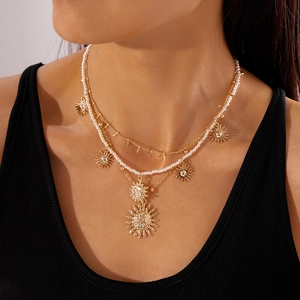 Detail of layered gold necklace set with pearls and bohemian sun pendants on model