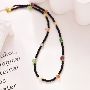 Detail of colorful seed bead necklace with faceted black beads and gold spacers on white pedestal