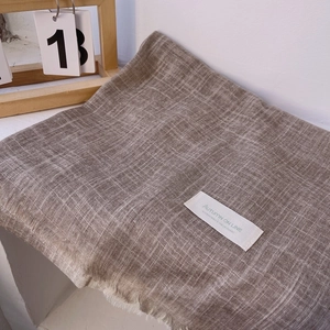 Detailed view of beige cotton linen scarf with plaid pattern, tassels, and a white label