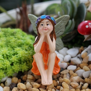 Macro shot of resin garden fairy figurine with orange dress and green wings