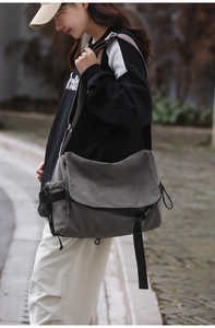 Detailed outdoor view of a grey canvas crossbody bag with black adjustable strap worn by model