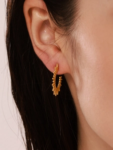 Close-up of C-shaped sunflower textured gold hoop earring worn on female ear model