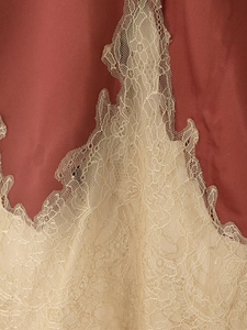 Detailed close-up of red satin fabric with beige floral lace trim and stitching