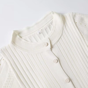 Detailed close-up of knit texture and embossed letter buttons on a cream collar dress