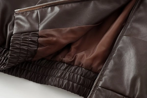 Close-up of dark brown faux leather bomber jacket with elastic hem and satin lining details