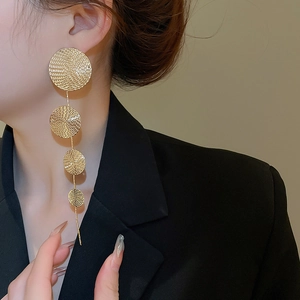 Detail of gold textured circular drop earrings with delicate chain tassels on model