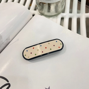 Elegant beige acetate hair claw clip with black border and rhinestones on a book page