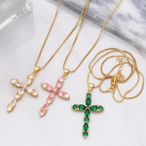 Detailed close-up of three gold cross necklaces with pink, green, and clear pear-cut stones