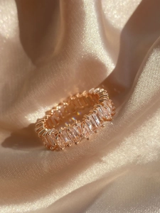 Close-up of a rose gold baguette-cut zircon eternity ring on champagne silk fabric