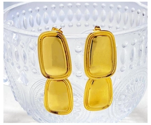 Detailed view of gold plated square pendant earrings hanging on a transparent glass bowl