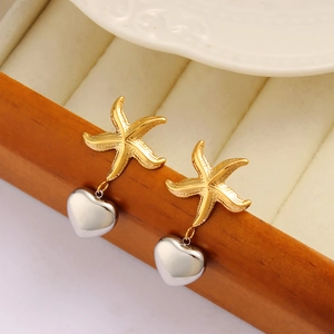 Fashionable gold starfish and silver heart drop earrings on a wooden jewelry box