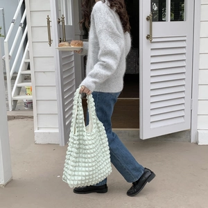 Detail showing light green bubble textured shoulder bag with 3D popcorn pattern on a model