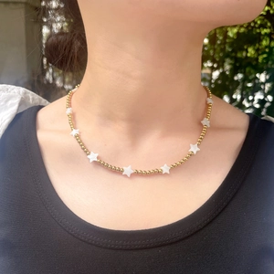 Golden beaded necklace with iridescent star shell charms worn on a woman's neck