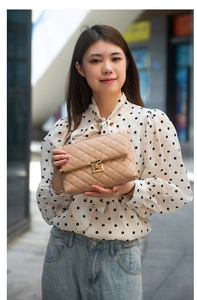 Quilted beige shoulder bag with gold chain strap shown on model in street setting